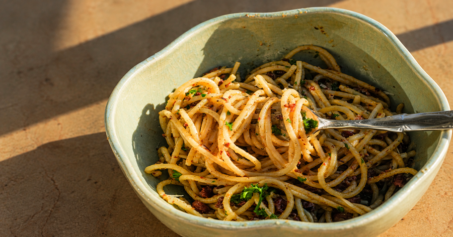 Bowl of Amuninni bronze-cut spaghetti coated in sauce with fresh parsley, a fork twirling the pasta