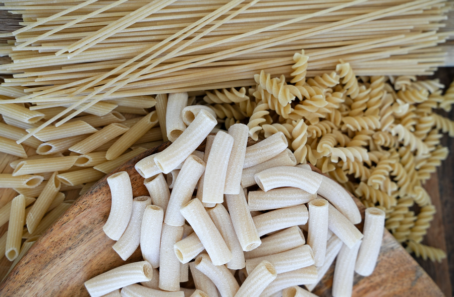 Amuninni organic pasta shapes – Spaghetti, Penne, Tortiglioni, and Fusilli – arranged on a wooden board.